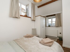 A bedroom with a bed, a window with curtains, a radiator, and a mirror. - Sheepwash Barn (Freshwater)