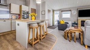 Una cocina moderna con una isla central, taburetes de bar, una mesa de comedor y una sala de estar con sofá y televisor.