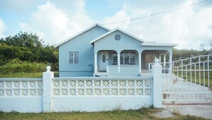 Une maison bleu clair avec une clôture blanche, un porche et un portail.