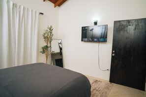 Ein Zimmer mit einem Bett, einem an der Wand montierten Fernseher, einer Tür und einer Pflanze.