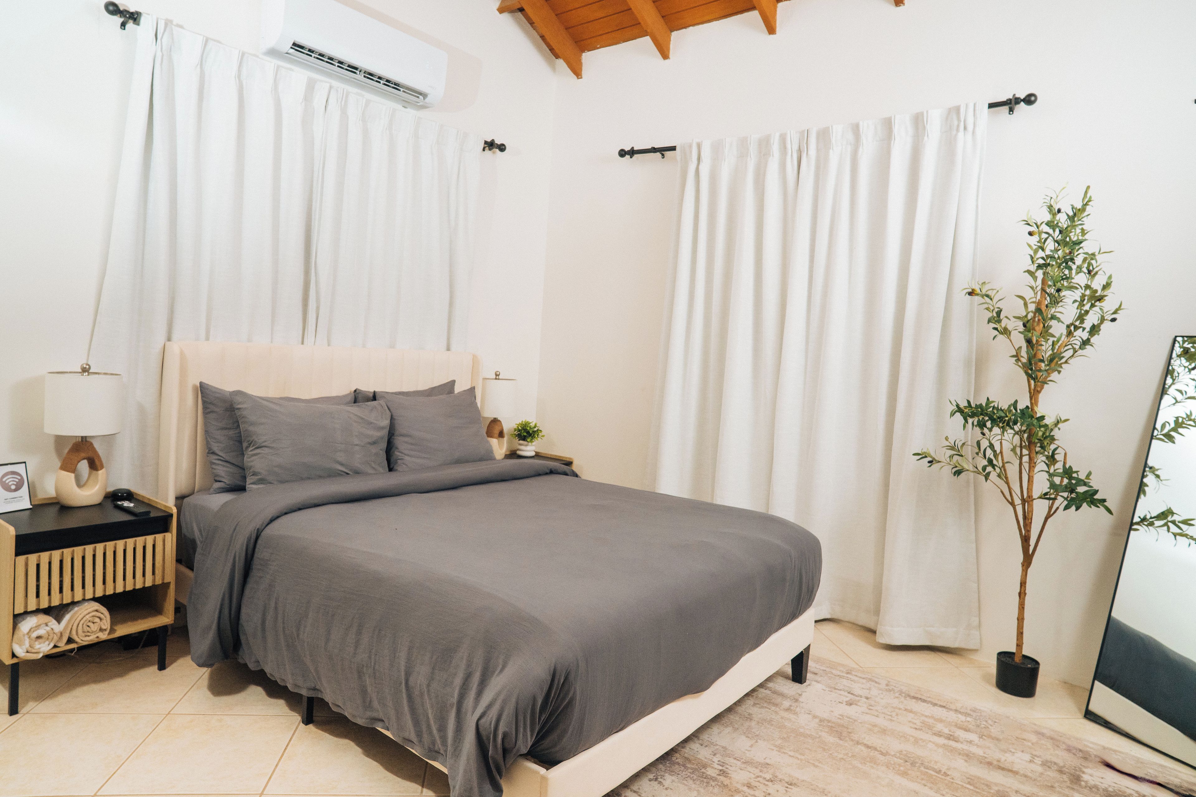 A bedroom with a bed, nightstands, a lamp, a potted plant, and a window with curtains.