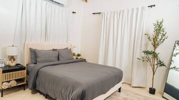 A bedroom with a bed, nightstands, a lamp, a potted plant, and a window with curtains.