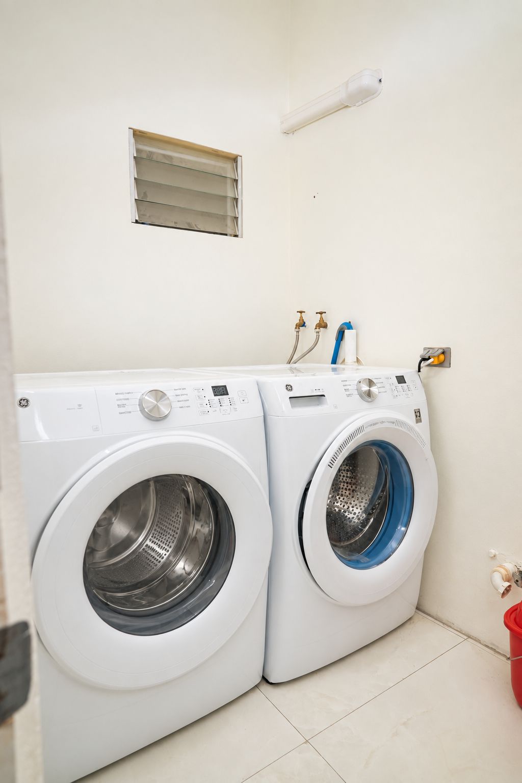 A laundry room with two front-loading washing machines and a small window above them.