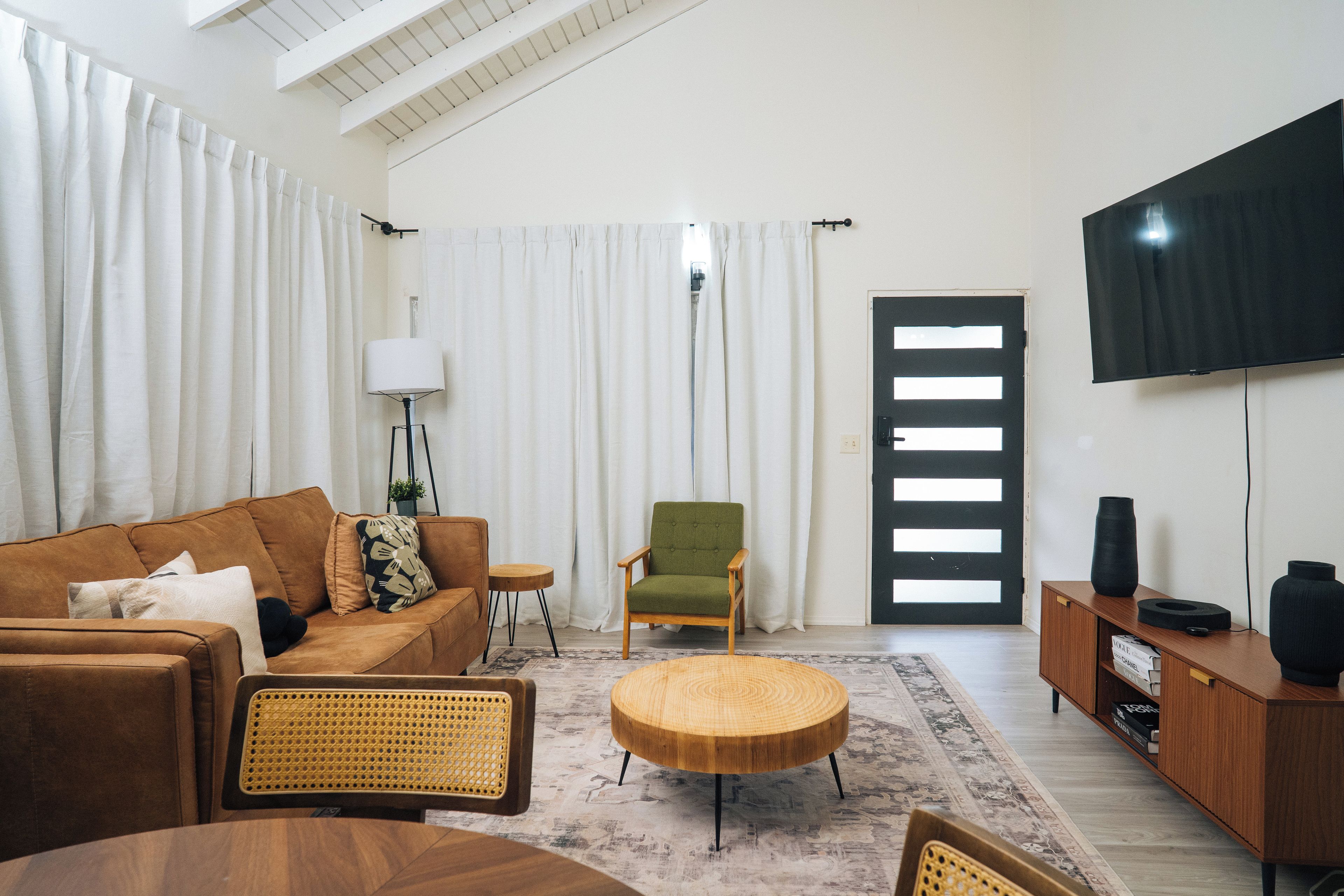 A living room with a brown sofa, a green armchair, a round wooden coffee table, a floor lamp, and a television on the wall.