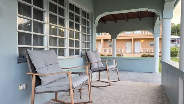 Un balcon agrémenté de deux fauteuils à bascule et d’une table en verre, donnant sur un immeuble qui possède également un balcon.