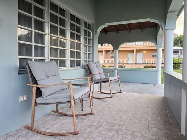 Ein Balkon mit zwei Schaukelstühlen und einem Glastisch, mit Blick auf ein Gebäude mit Balkon.