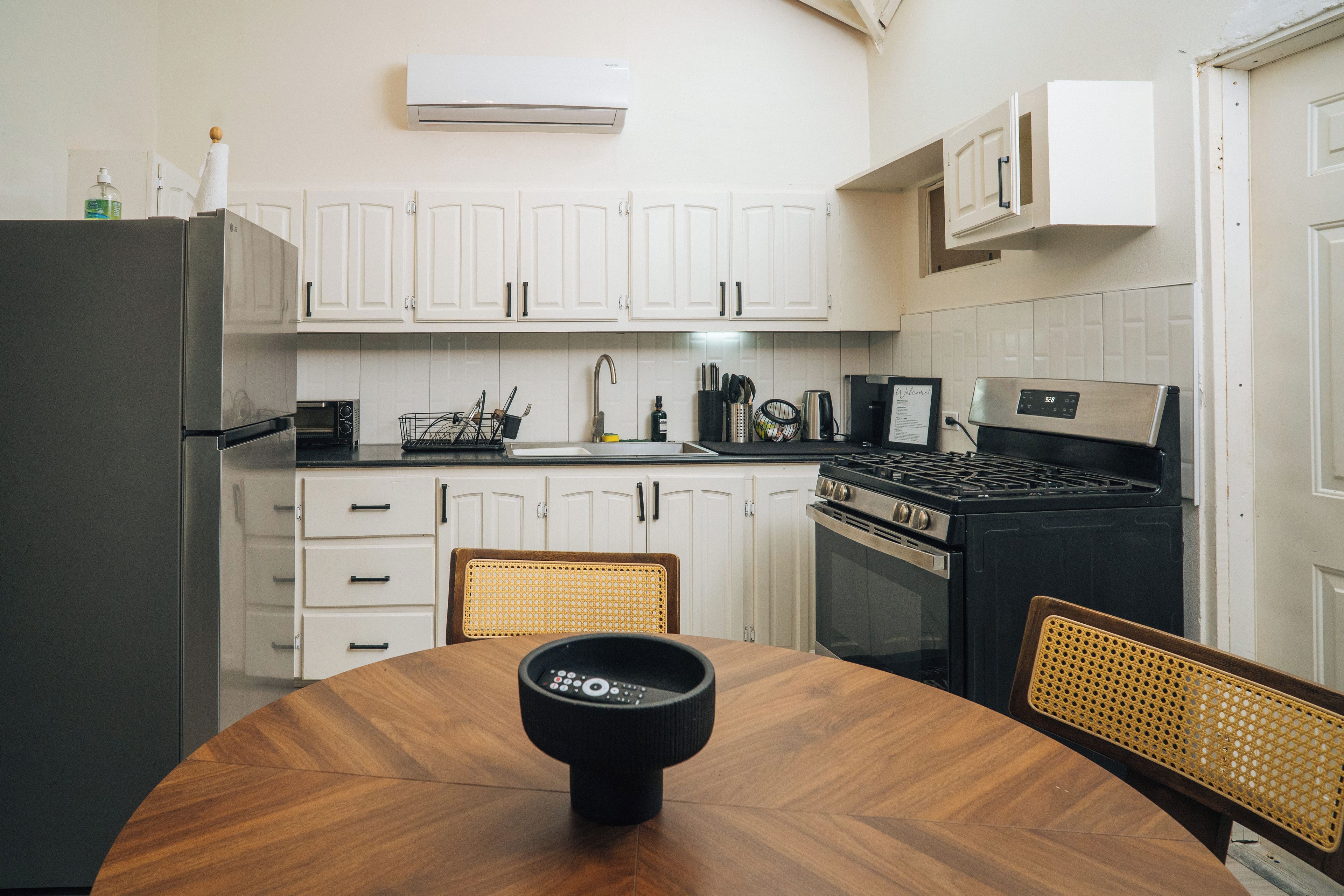 A kitchen with white cabinets, a black stove, a dining table with chairs, and an air conditioning unit above the cabinets.