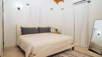 Ein Schlafzimmer mit Bett, Vorhängen, einem Nachttisch, einer Lampe und einer Klimaanlage.