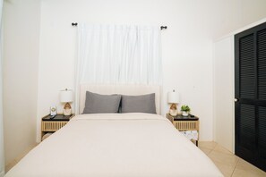 Een hotelkamer met een bed, twee nachtkastjes met lampen, een raam met gordijnen en een deur.