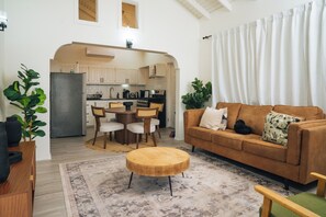 Una sala de estar moderna con un sofá marrón, una mesa de centro redonda de madera y un comedor con una mesa y sillas blancas.