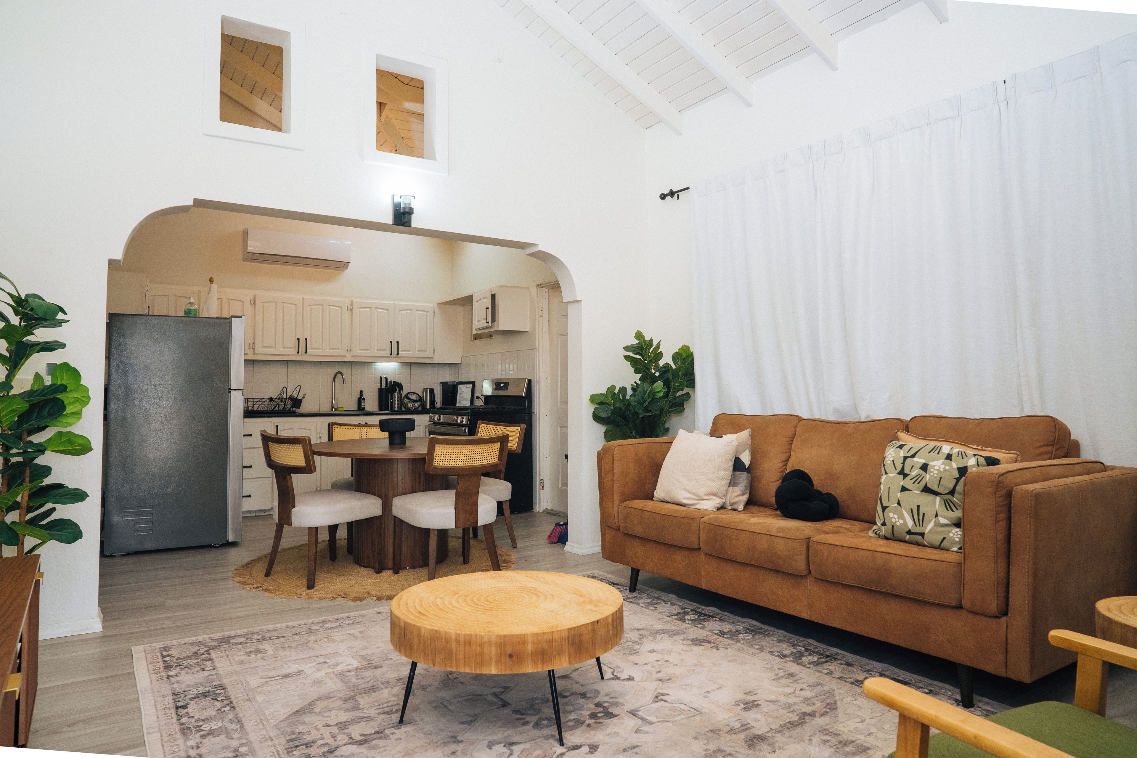 A modern living room with a brown sofa, a wooden coffee table, and a dining area with a kitchen in the background.