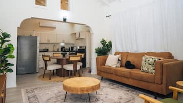 A modern living room with a brown sofa, a wooden coffee table, and a dining area with a kitchen in the background.