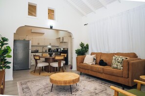 Una sala de estar moderna con un sofá marrón, una mesa de centro de madera y un comedor con una cocina al fondo.