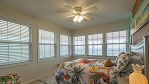 Ein Schlafzimmer mit einem Bett, einem Deckenventilator und großen Fenstern.
