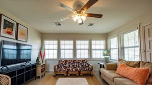 Ein Wohnzimmer mit Fernseher, Sofa, Hocker und Deckenventilator.
