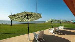 Eine Terrasse mit weißen Adirondack-Stühlen und Tarnfarb-Sonnenschirmen, mit Blick auf ein Gewässer.