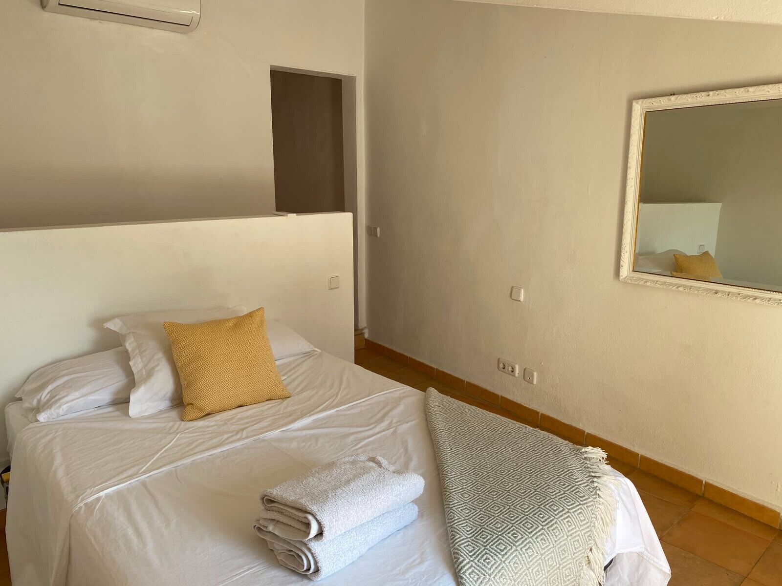 A hotel room with a bed, a mirror, and a wall-mounted air conditioning unit.
