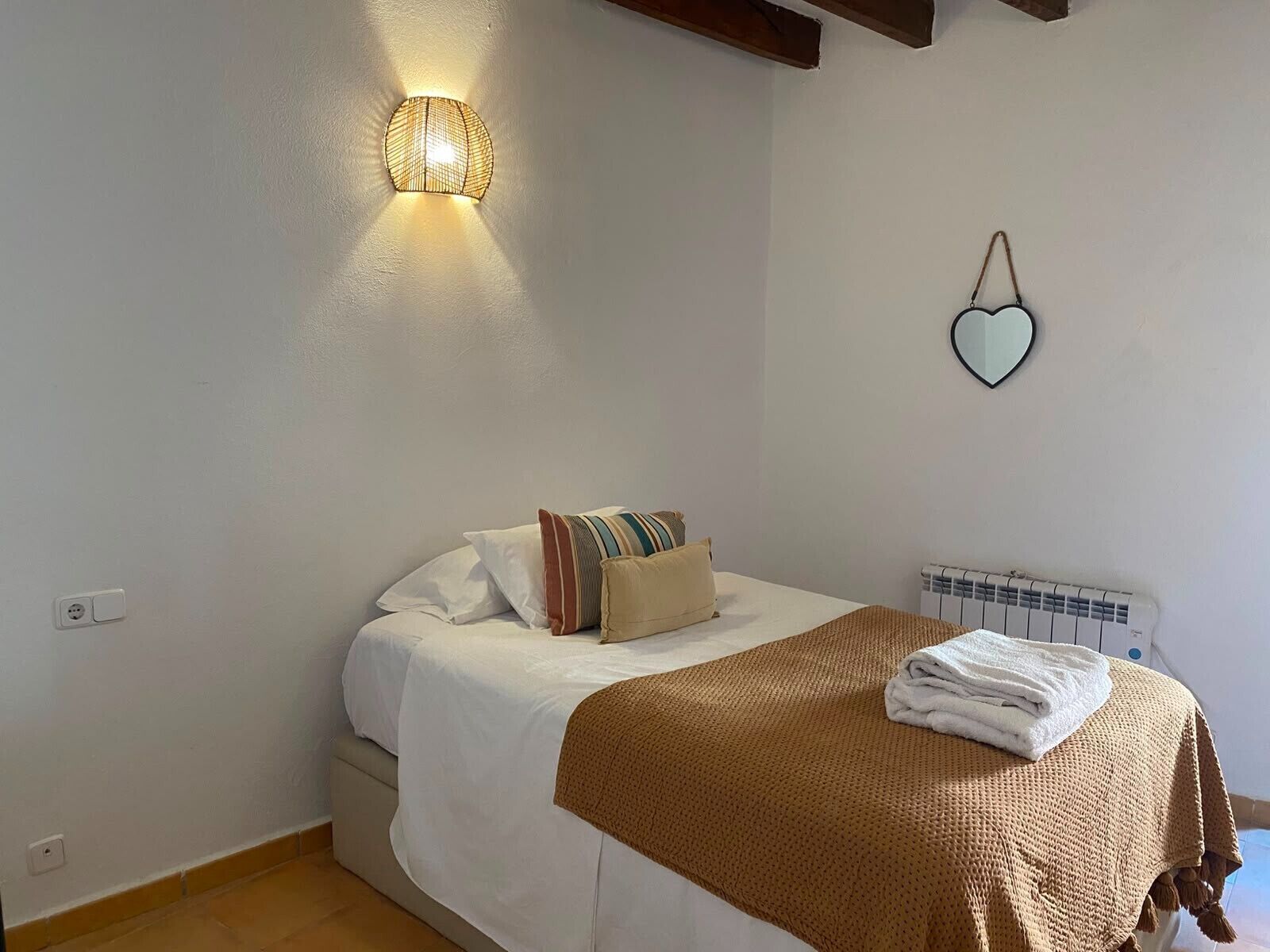 Un dormitori amb un llit, una làmpada penjada a la paret, un radiador i una decoració amb forma de cor.