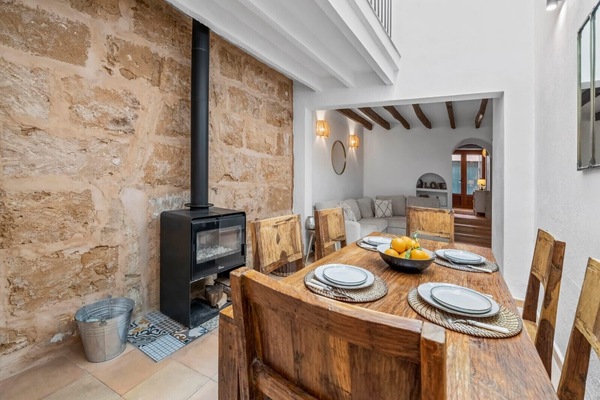 Dining area with a wooden table and a wood-burning stove, connected to a cosy living room in a renovated Mallorcan house.