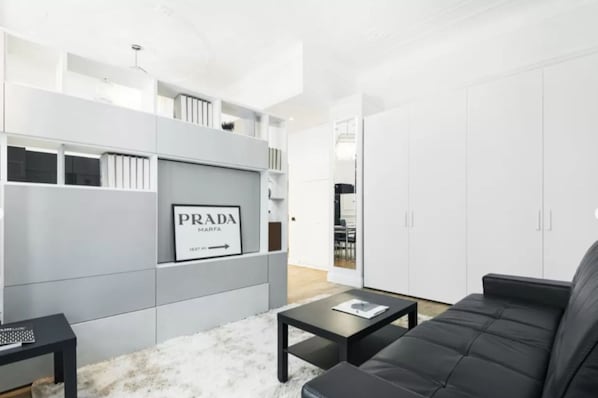 A modern living room with a black leather sofa, a coffee table, and a grey shelving unit with a Prada sign.