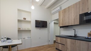 A modern kitchen with wooden cabinets, a black countertop, and a built-in microwave. There is a white dining table with chairs and a shelf with glassware. - Centro Bligny B - Lovely Studio in Bocconi Area (Milan)