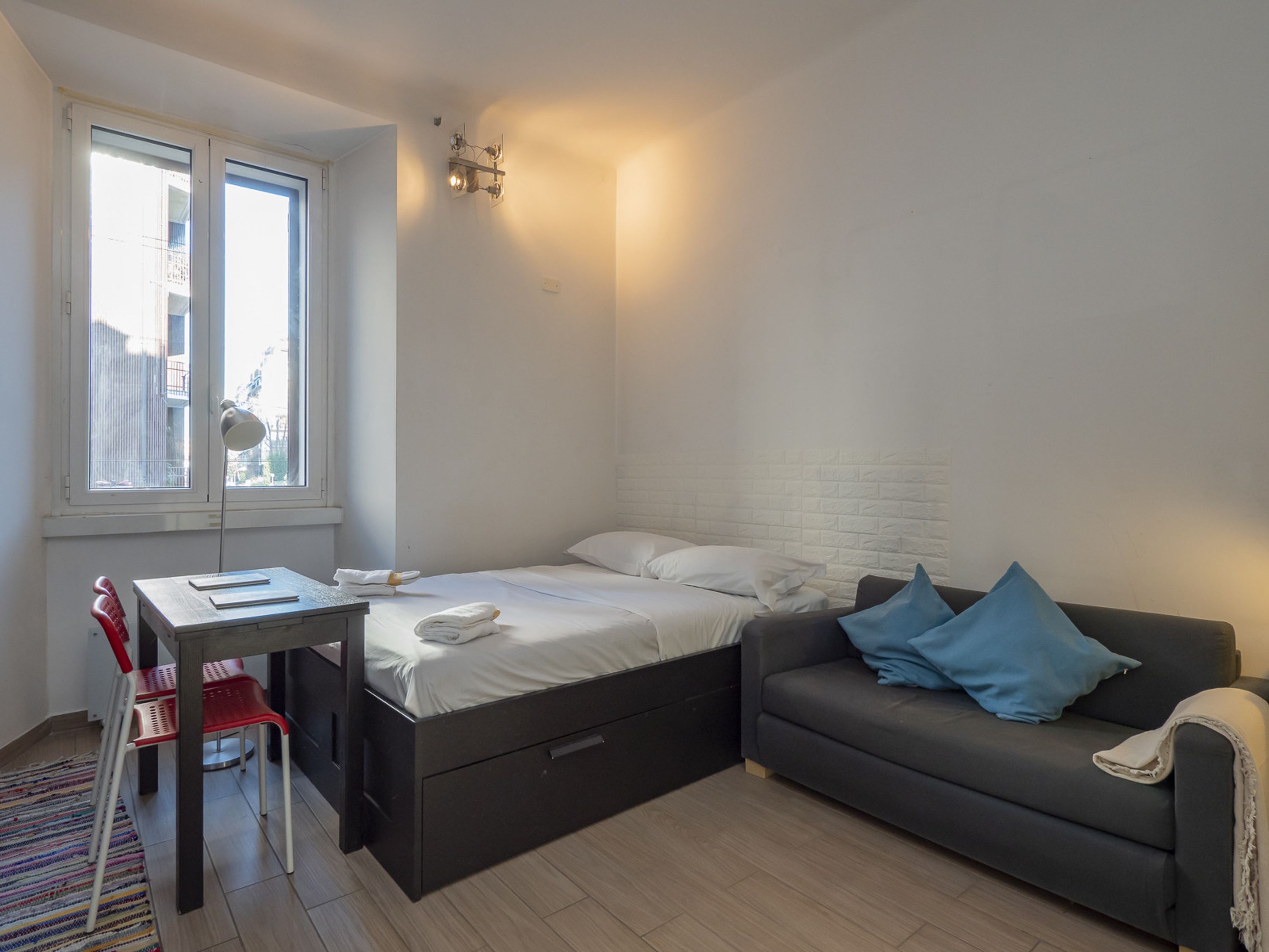 A compact room with a bed, a small desk, a chair, and a sofa.