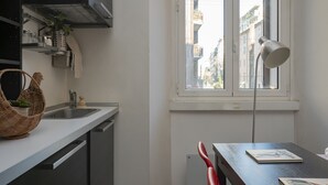 A kitchen with a window, a red chair, and a table with books. - Centro Bligny B - Lovely Studio in Bocconi Area (Milan)