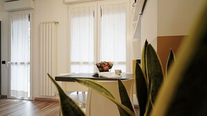 Een eetruimte met een tafel, stoelen, een schaal fruit en een raam met gordijnen.