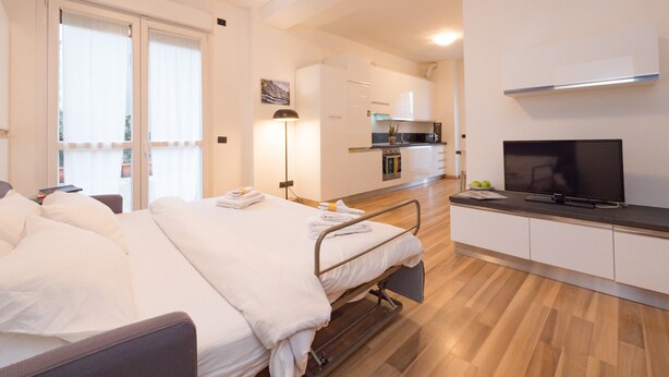 Een hotelkamer met een bed, nachtkastje, lamp en een kitchenette met een televisie.