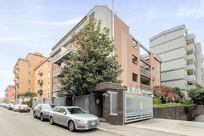 A modern apartment building with a gated entrance, parked cars, and a tree in front. - Candiani D2 Monolocale (Milan)