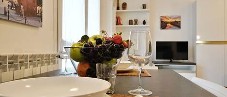 A dining table with a bowl of fruit, a wine glass, and cutlery.