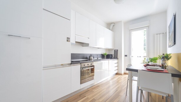 A modern kitchen with white cabinets, a black countertop, and a wooden floor. - Palazzo Candiani - Deluxe Studio With Terrace (Milan)