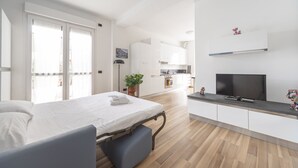 A modern hotel room with a bed, a TV, a small kitchenette, and a balcony with a sliding door. - Palazzo Candiani - Deluxe Studio With Terrace (Milan)