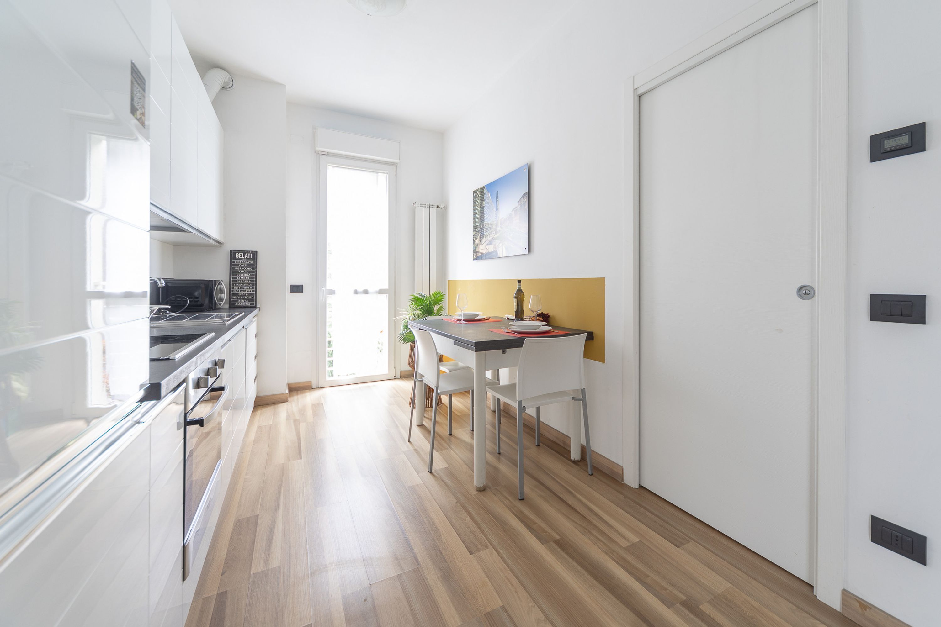 A modern kitchen with white cabinets, a black stove, and a dining area with a white table and chairs.