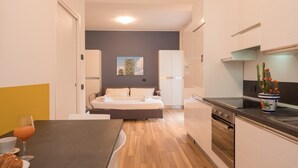 Cocina moderna con comedor, cama y pequeña mesa con un croissant y jugo.