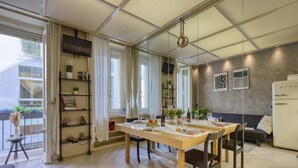 A modern dining area with a wooden table set for four, a sofa, and a refrigerator. - Cerva - Stylish 1 Bedroom Close to Duomo (Milan)