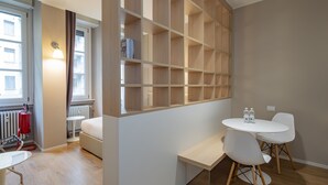 Ein modernes Hotelzimmer mit einer Holzbibliothek, einem runden Esstisch mit weißen Stühlen, einem Bett mit weißem Kopfteil und einer Heizung.