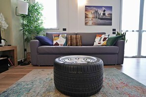 A living room with a grey sofa, colorful cushions, a large window, and a plant. - Palazzo Candiani - Modern Split-level 1BR Apartment Near Politecnico (Milan)