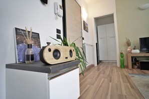 Una sala moderna con suelo de madera, una mesa de centro con un jarrón y un libro, una planta verde y un televisor sobre un mueble.