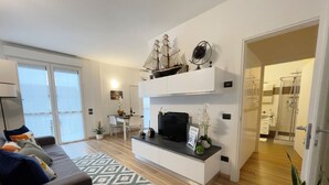 Ein modernes Wohnzimmer mit einer Couch, einem Couchtisch und einem gemusterten Teppich. Es gibt einen Essbereich mit Tisch und Stühlen, sowie eine Küchenzeile mit Arbeitsplatte und Schränken.