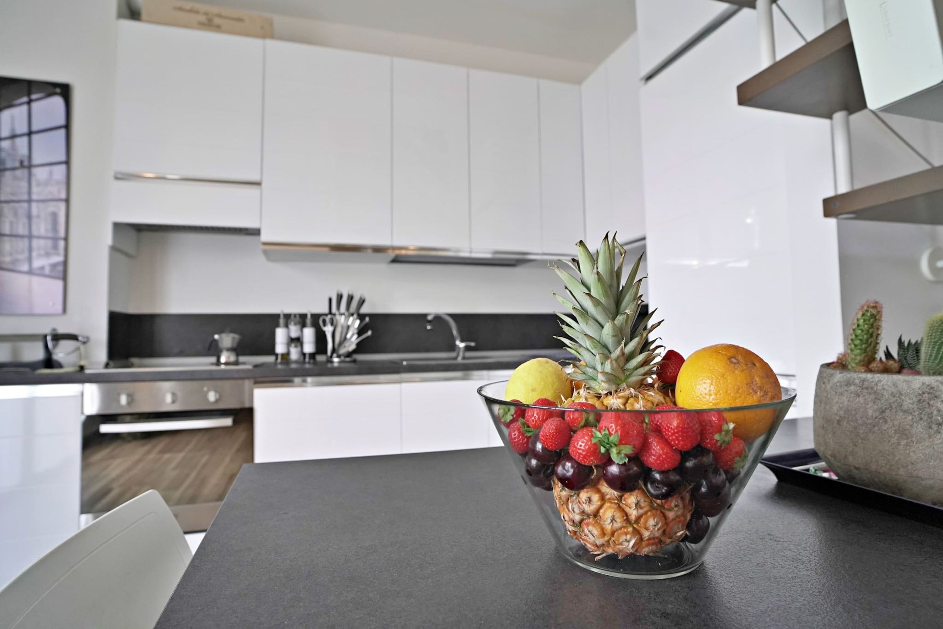 Una cucina moderna con mobili bianchi, elettrodomestici in acciaio inossidabile e una ciotola di frutta sul bancone.