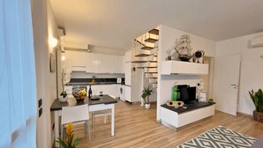 Eine moderne Küche mit weißen Schränken, ein Essbereich mit Tisch und Stühlen sowie ein Wohnzimmer mit einem gemusterten Teppich.