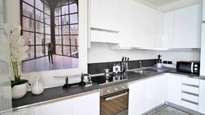 A modern kitchen with white cabinets, a black countertop, and stainless steel appliances. - Palazzo Candiani - Modern Split-level 1BR Apartment Near Politecnico (Milan)