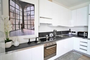 A modern kitchen with white cabinets, a black countertop, and stainless steel appliances. - Palazzo Candiani - Modern Split-level 1BR Apartment Near Politecnico (Milan)
