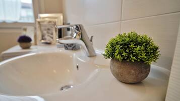 Un lavamanos de baño con una pequeña planta en maceta, un espejo y un cuadro en el mostrador.