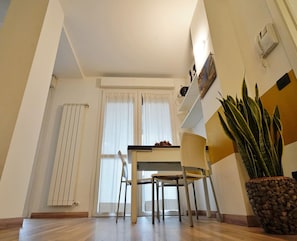 Et spiseområde med et bord, stole, en radiator, en potteplante og en telefon monteret på væggen.