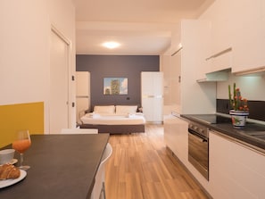 Cocina moderna con comedor, cama y pequeña mesa con un croissant y jugo.