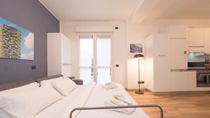 Una habitación de hotel moderna con una cama grande, una mesita de noche, una lámpara de pie y vistas a la ciudad a través de la ventana.