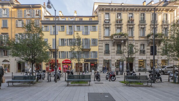 Une place publique avec des bancs, des trottinettes et des piétons.