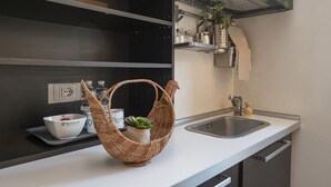 Een moderne keuken met een wit aanrecht, een RVS spoelbak en een hangende rieten mand met een plantje.